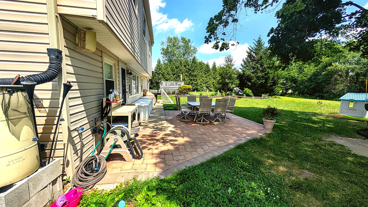 Bright, spacious backyard paver patio bordered by mature trees and green lawn, Turnersville NJ